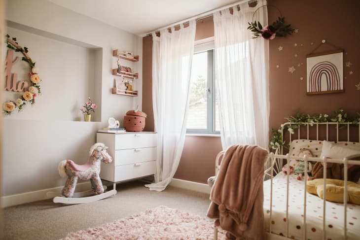 kid's bedroom with white and brown walls. white iron bed frame, plush rocking horse, white dresser, white sheer curtains
