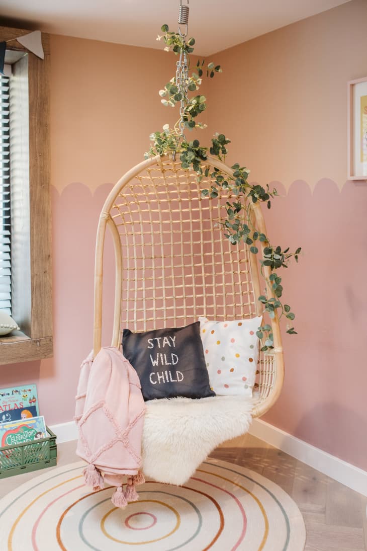 wicker hanging swing in kids playroom. Blush colored walls, faux ivy on swing. Pillow on swing says "stay wild child"