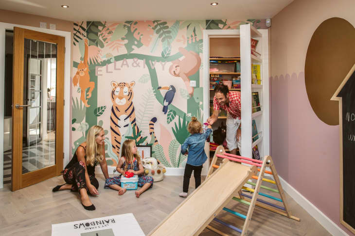 Family in kids playroom with mural and secret bookcase door. Wooden slide in foreground