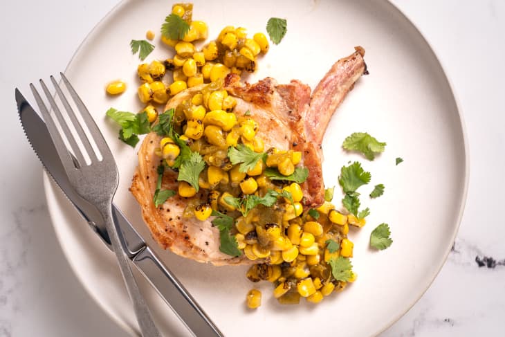 Pork chop with corn salsa on a white plate with knife and fork