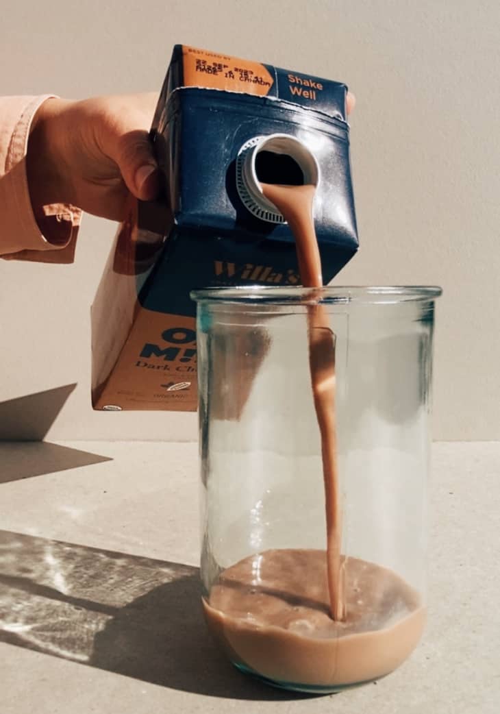 person pouring chocolate oat milk into a glass