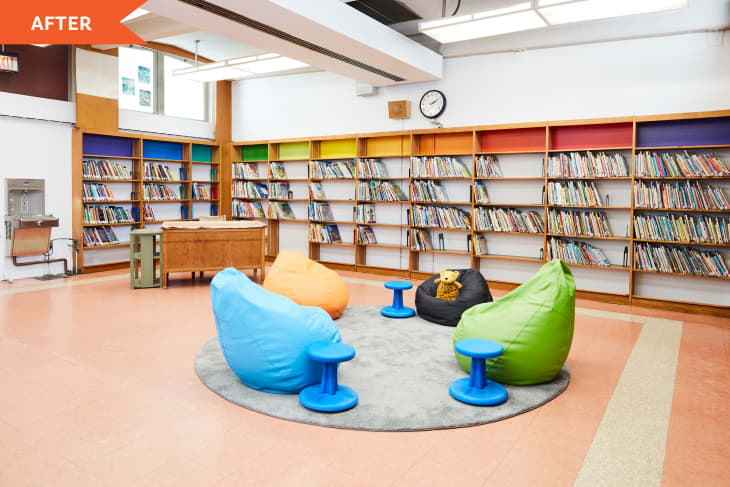 A colorful and bright reading nook in the Henry Houston School Library with the librarian's desk and freshly painted bookshelves in the background. In partnership with Benjamin Moore, the top shelf features the colors Ruby Red, Orange Burst, Citrus Blast, Bright Yellow, Outrageous Orange, Lizard Green, Brilliant Blue, Scandinavian Blue, Rolling Hill Green, Apple Green.