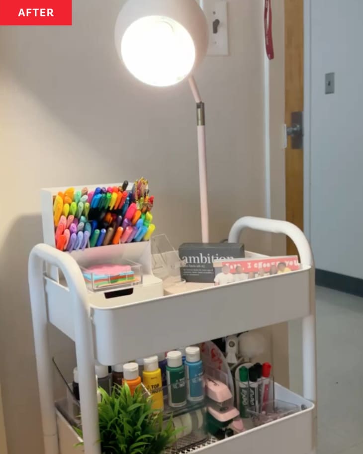 white rolling card with art supplies organized on shelf and desk lamp on top