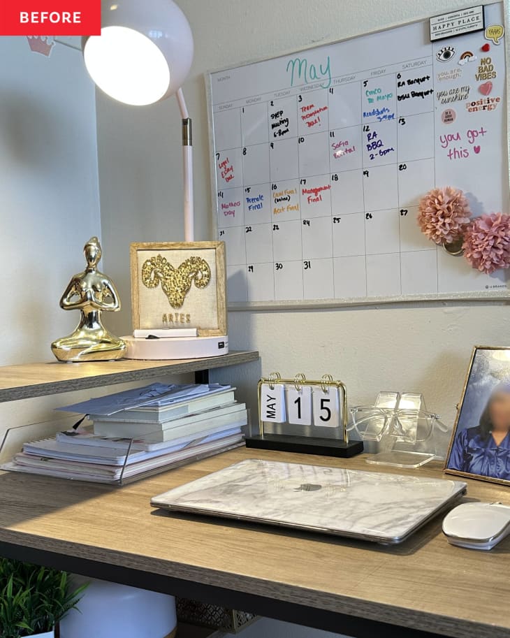 dry erase white board calendar on wall above desk with computer and gold buddha statue, white round desk lamp and stacks of papers