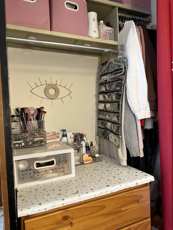 detail of makeup, toiletries closet area in dorm room, pink storage bins above, hanging clothes