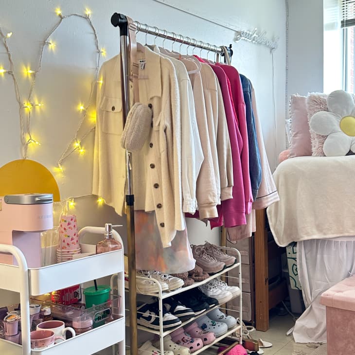 dorm room with white, pink accents, combined clothing and shoe rack, string lights, window