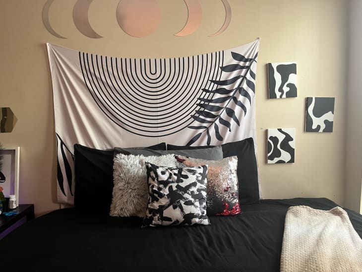 black sheets, black and white curved line tapestry above bed, black and white squiggly art, beige throw blanket, black and white throw pillows, moonscape above bed