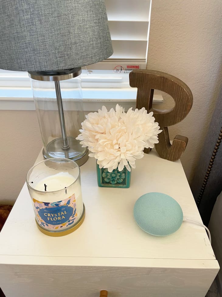 Small floral arrangement on white nightstand with lamp, Wooden "R" letter, small speaker and candle.