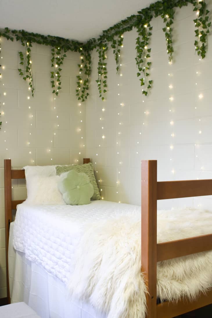 White painted cinder block room with an elevated bed and string lights and plant decorations.