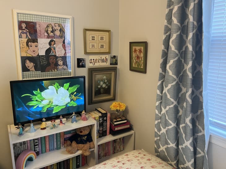 princess pop art, tv, low white bookshelf, colorful books, yellow flowers, pictures on wall, princess figurines, floral sheets, blue and white diamond pattern curtain