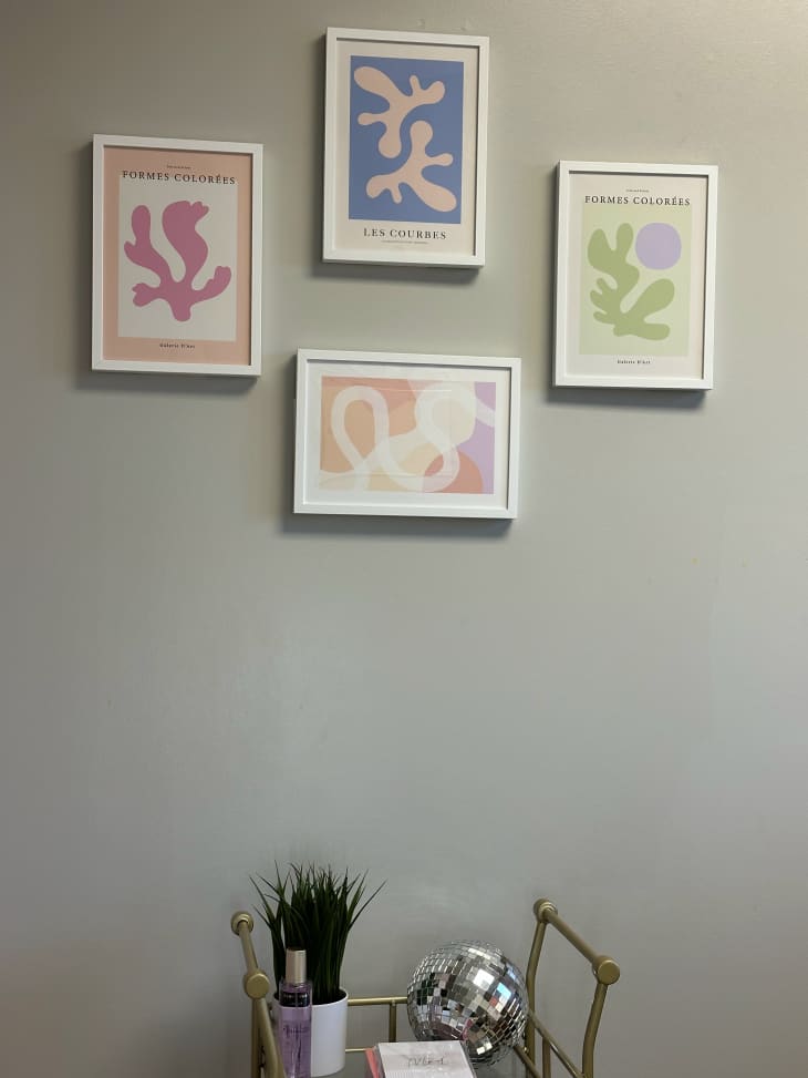 Four framed pieces of artwork on a grey wall above a decorative cart.