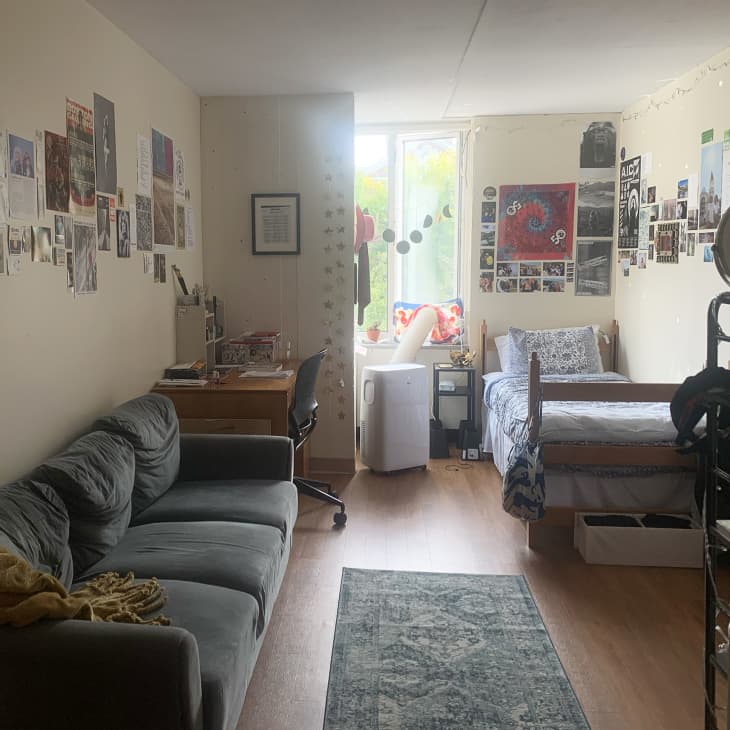 off-white dorm room with gray sofa, single wood frame bed with blue and white linens, and lots of art/pictures on the walls