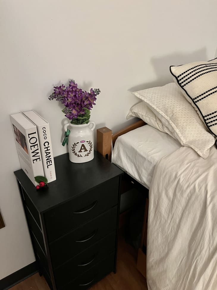 black three drawer side table next to bed with lavender in vase with A on it and books standing up