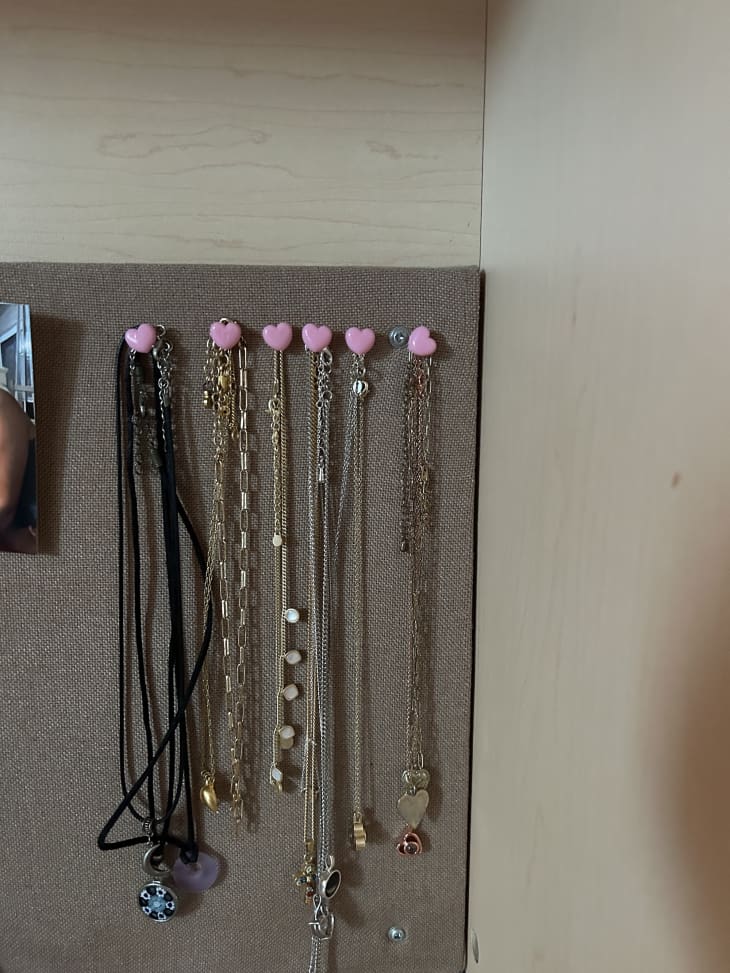 Necklaces hang from pink thumbtacks.