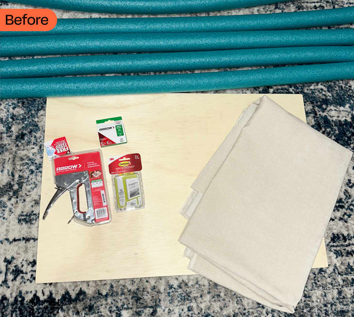 Supplies laid out to make pool noodle headboard including staple gun, staplers, fabric, wooden backing and pool noodles.