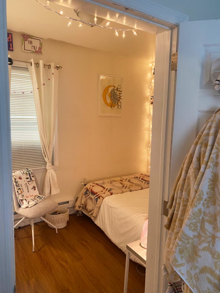 Dorm room with lit string lights, white walls, wood floor, window with white curtains