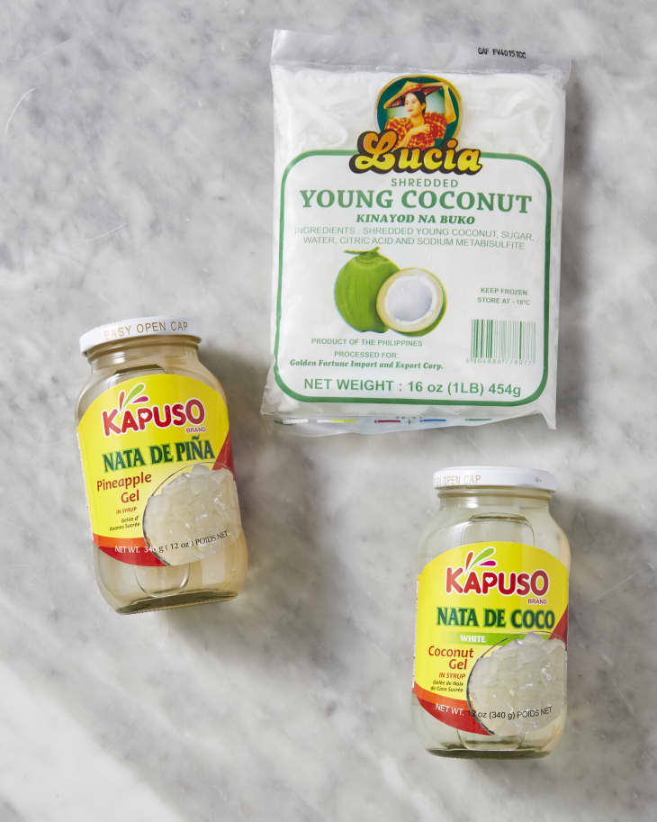 A trio of filipino ingredients: a jar of nata de coco, a jar of nata de piña, and a bag of young coconut on a marble surface
