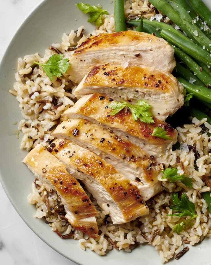 a sliced moist and tender chicken breast with a perfect sear on a bed of wild rice and a side of green beans