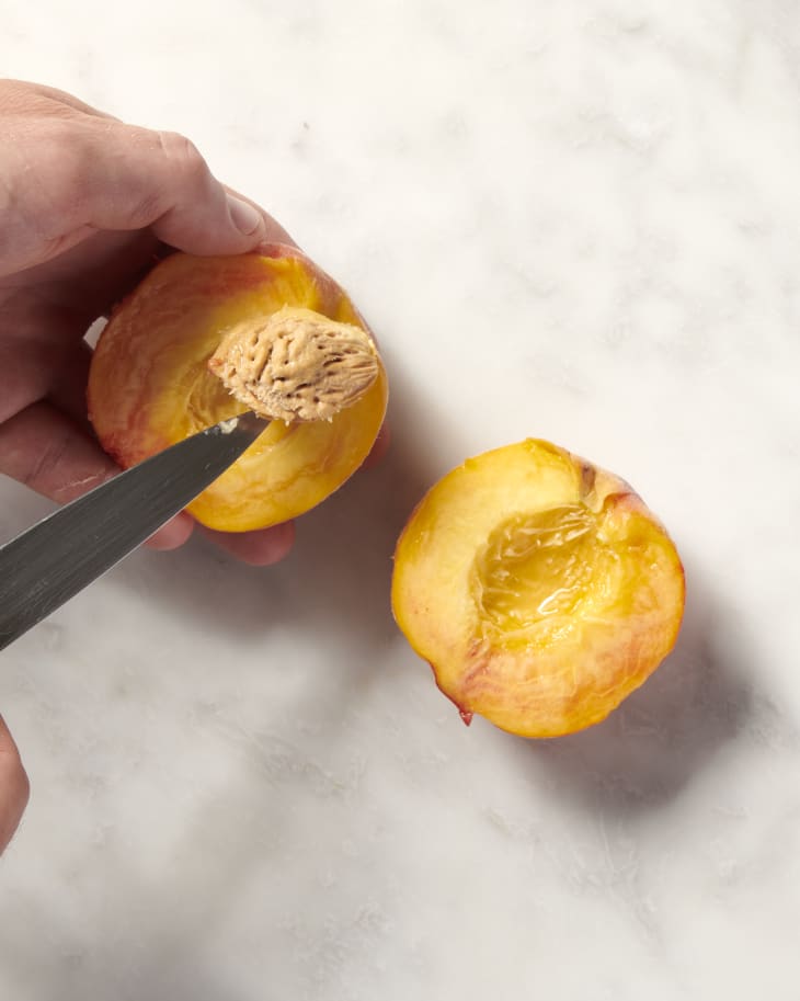 a halved peach with the pit being removed by prying with a paring knife