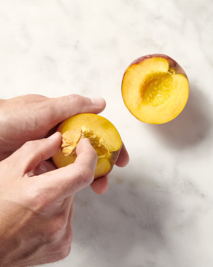 a halved peach with the pit being removed by hand