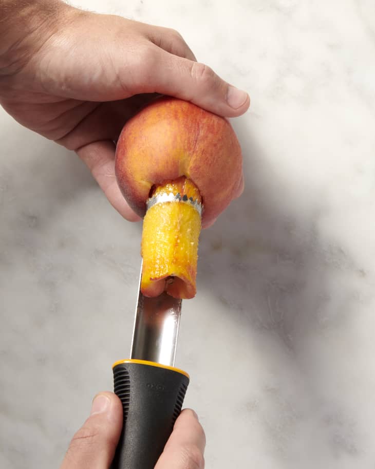 a halved peach with the pit being removed with a peach pitting tool