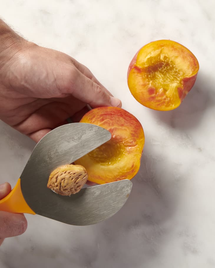 a halved peach with the pit being removed with a peach pitting tool