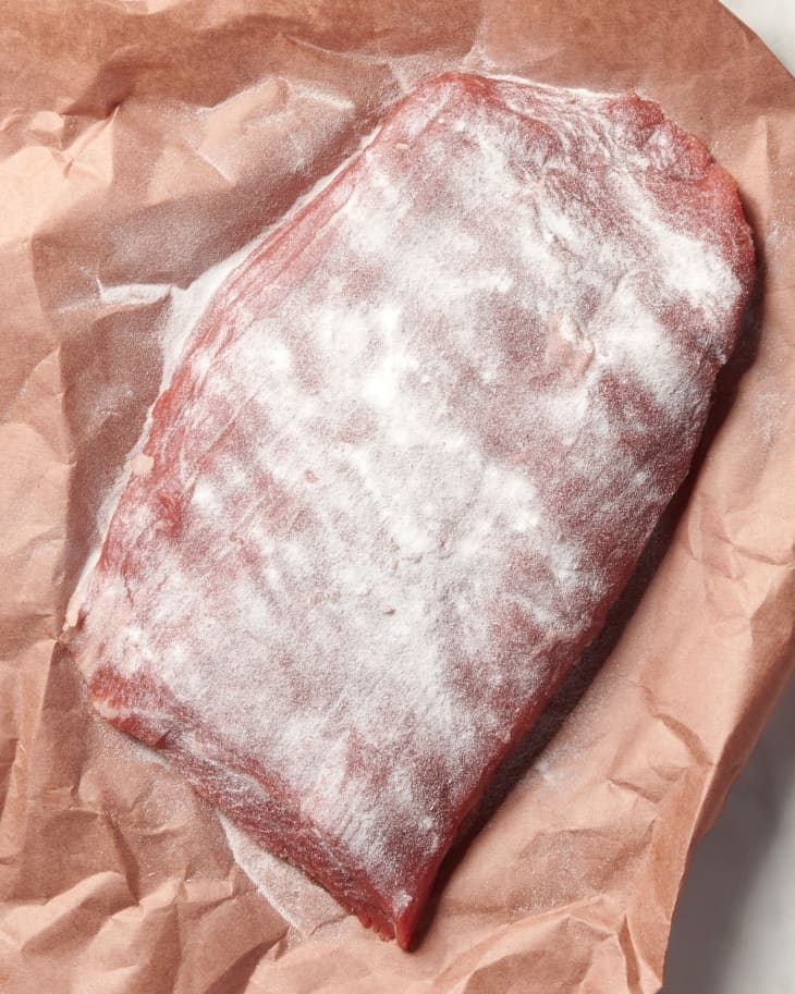 photo of a raw steak on butcher paper with a layer of tenderizing powder sprinkled on top