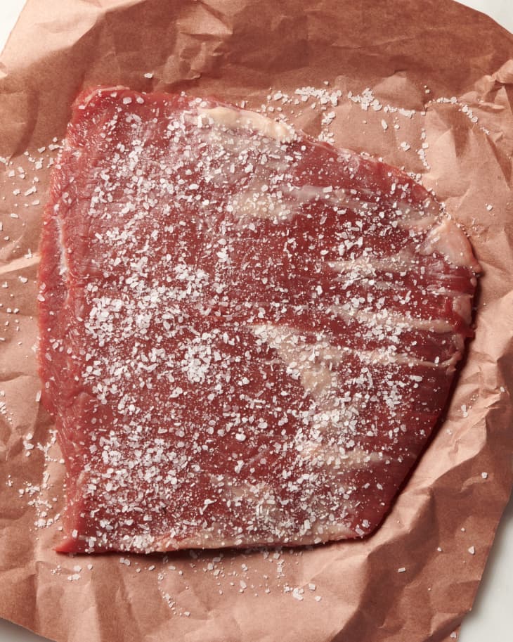 photo of a raw steak on butcher paper with a layer of salt sprinkled on top
