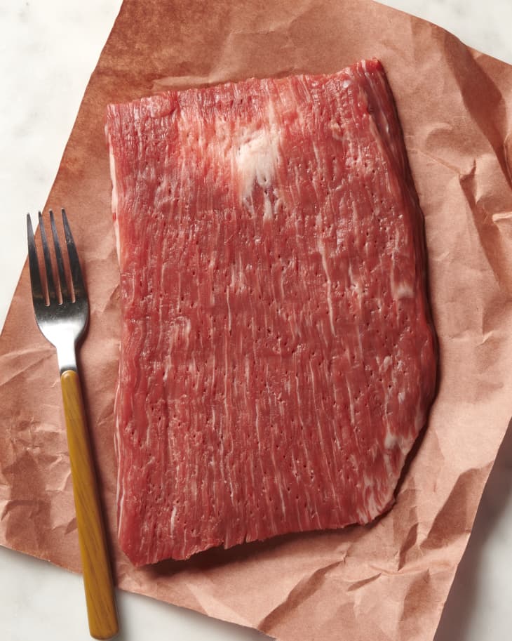 photo of a raw steak on butcher paper that has been tenderized with a fork with the fork laying next to the steak