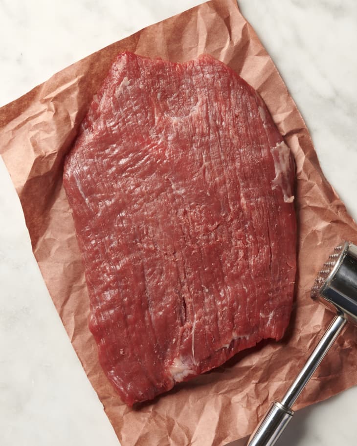 photo of a raw steak on butcher paper that has been tenderized with a meat mallet, the mallet is in the corner