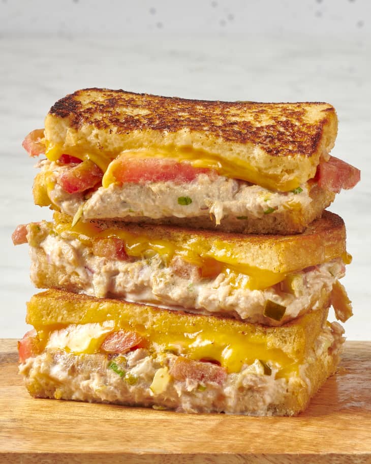 a stack of three tuna melt sandwich halves showing melty, gooey cheese and ripe, red tomatoes on a butting board