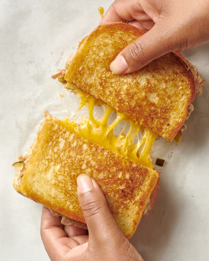 a halved cheesy tuna melt sandwich with perfectly toasted bread being pulled apart showing a delectable cheese pull between the two halves