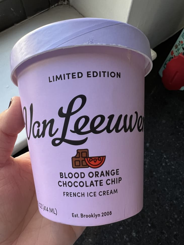 Someone holding a pint of Van Leeuwen's blood orange chocolate chip ice cream.