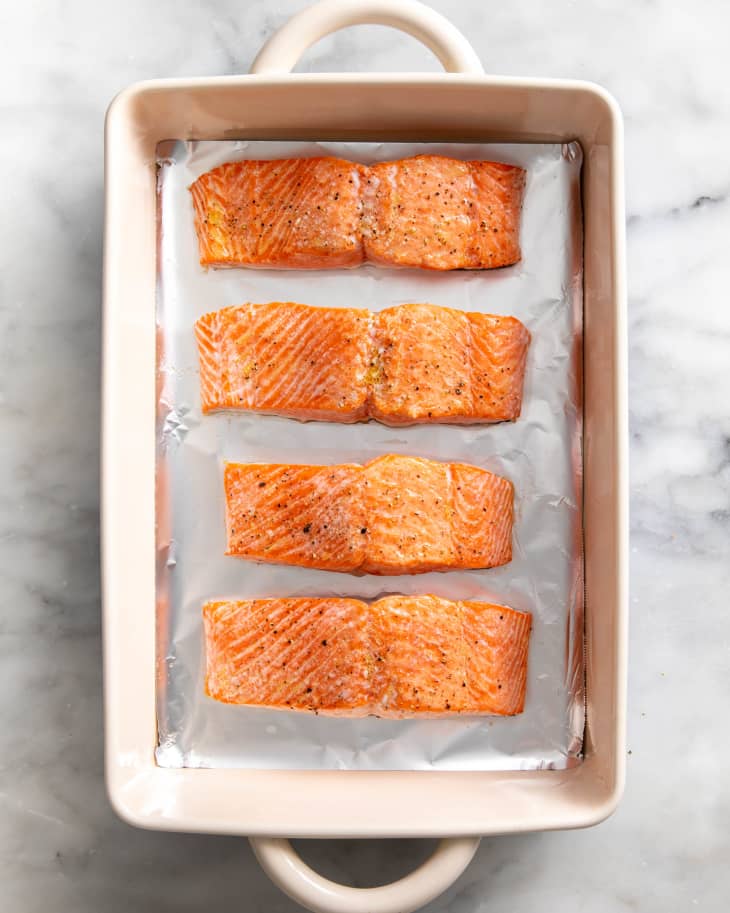 four pieces of baked salmon lays on foil paper in a baking dish placed on a marble surface
