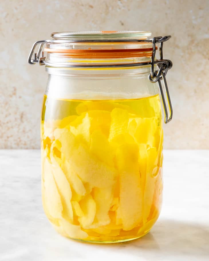 lemon peels in a latch jar soaking in vodka placed on a marble surface with a rustic backdrop