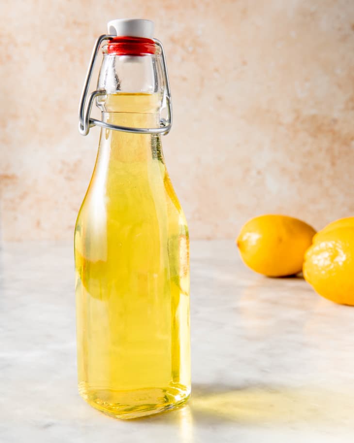 latch bottle of limoncello place on a marble surface with two lemons in the background and a rustic backdrop