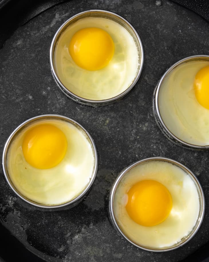 4 eggs in process on a skillet each in a separate egg rings, yolk intact