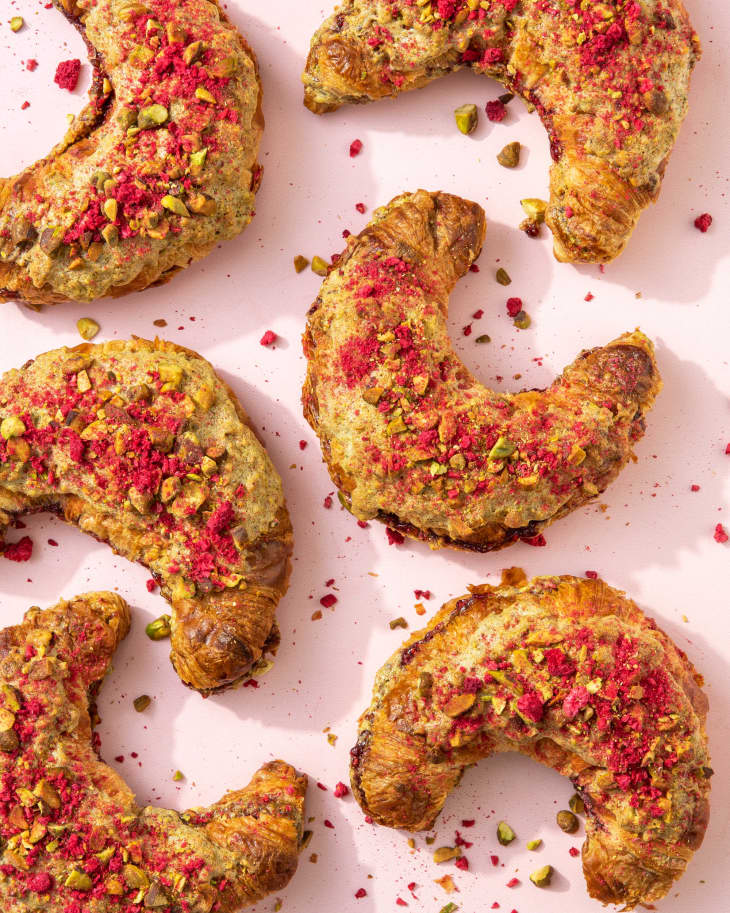 six croissants placed on a pink background with crumbs of pistachio and raspberry on the surface