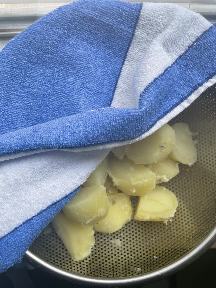 Cooked potatoes in a strainer under a blue tea towel