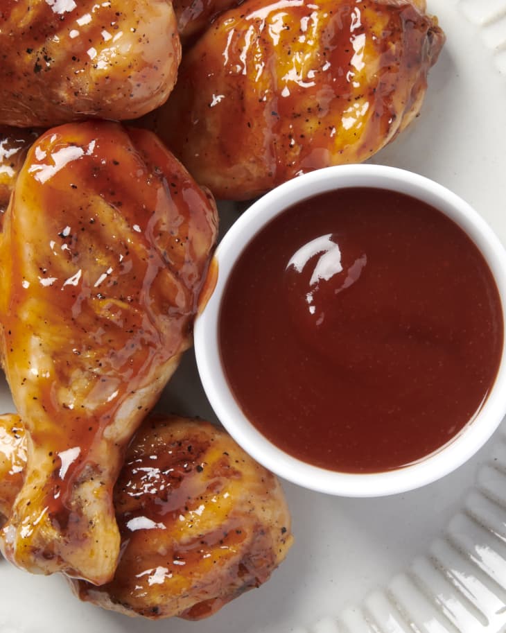 close up overhead shot of barbecue chicken with a white bowl of honey barbecue sauce next to it on a white plate