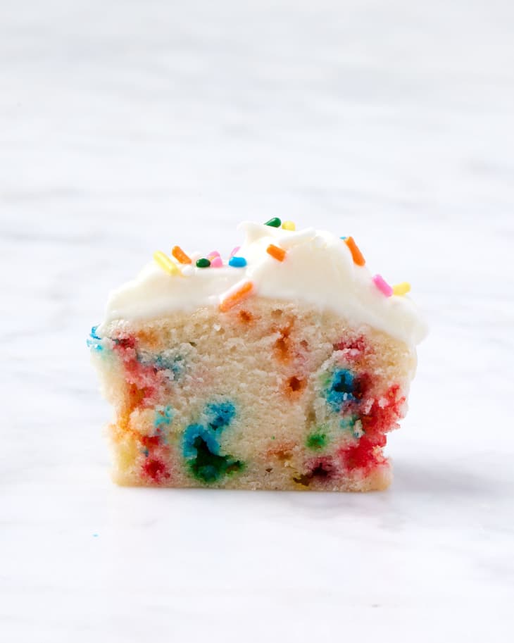 half of funfetti cupcake showing the inside with frosting and sprinkles on top placed on a marble surface