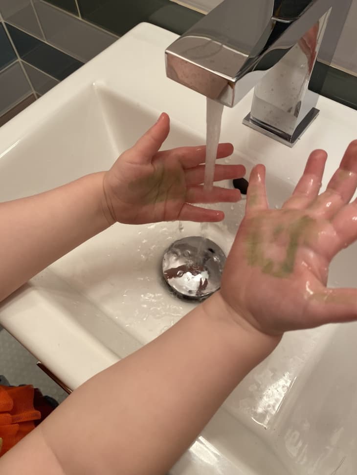 A child washing their hands with a green drawing on a hand