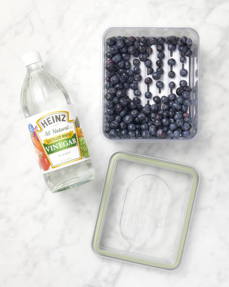 overhead shot of a container of blueberries, a bottle of vinegar next to it, and a container cover on a marble surface