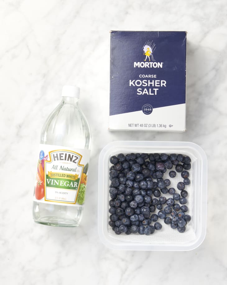 overhead shot of a container of blueberries, a bottle of vinegar next to it, and a box of salt on a marble surface