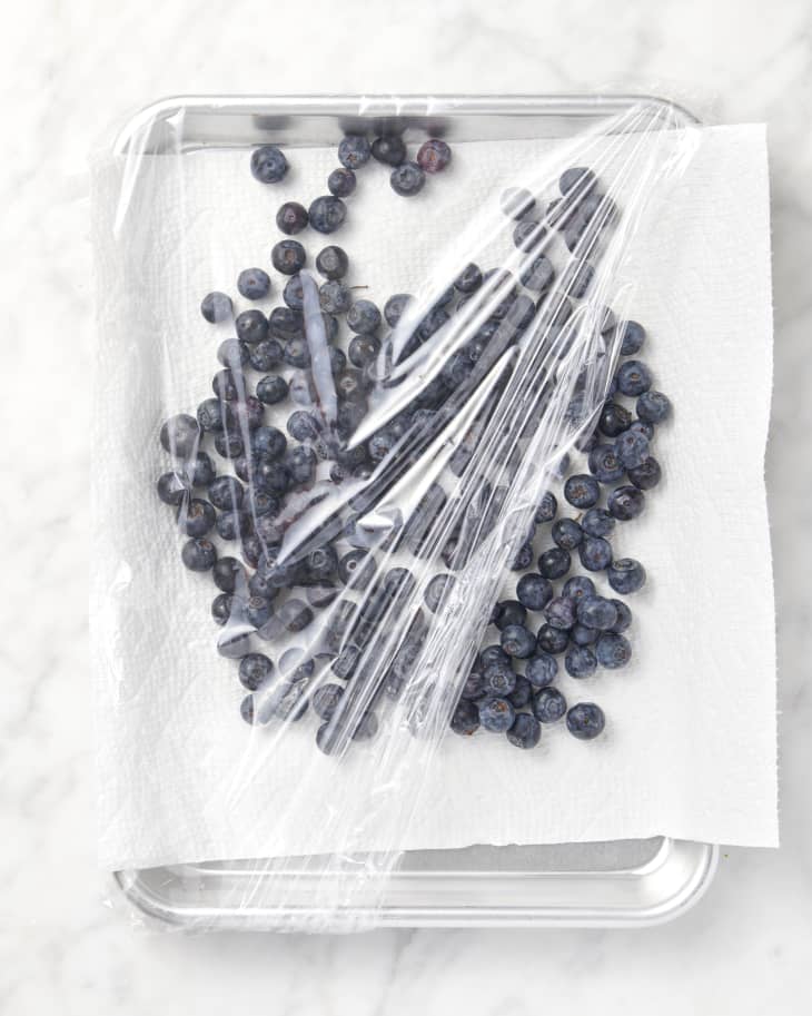 overhead shot of blueberries on marble surface in a container lined with paper towel and a plastic wrap over it
