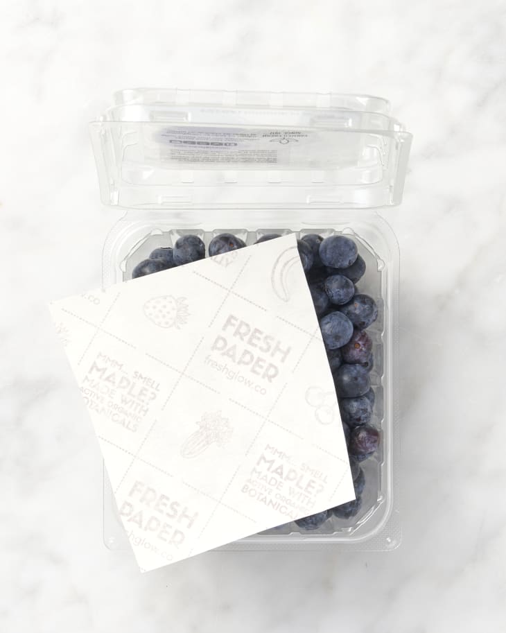 overhead shot of blueberries on marble surface in a container with a fresh paper on top