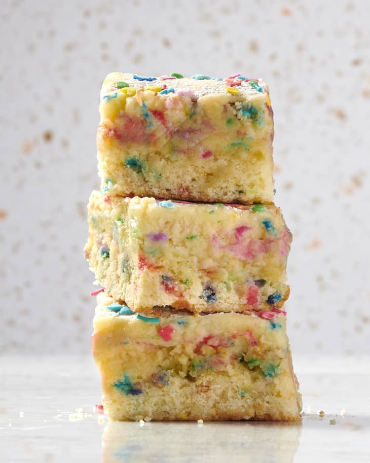 shot of 3 squared slices of gooey butter cake stacked on top of each other on a marble surface and a speckled backdrop