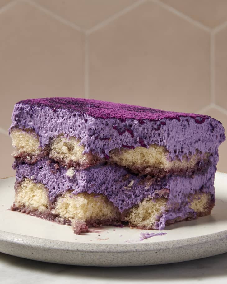 closeup shot of a slice of ube tiramisu on white textured plate thats on a marble surface and brownish tile background
