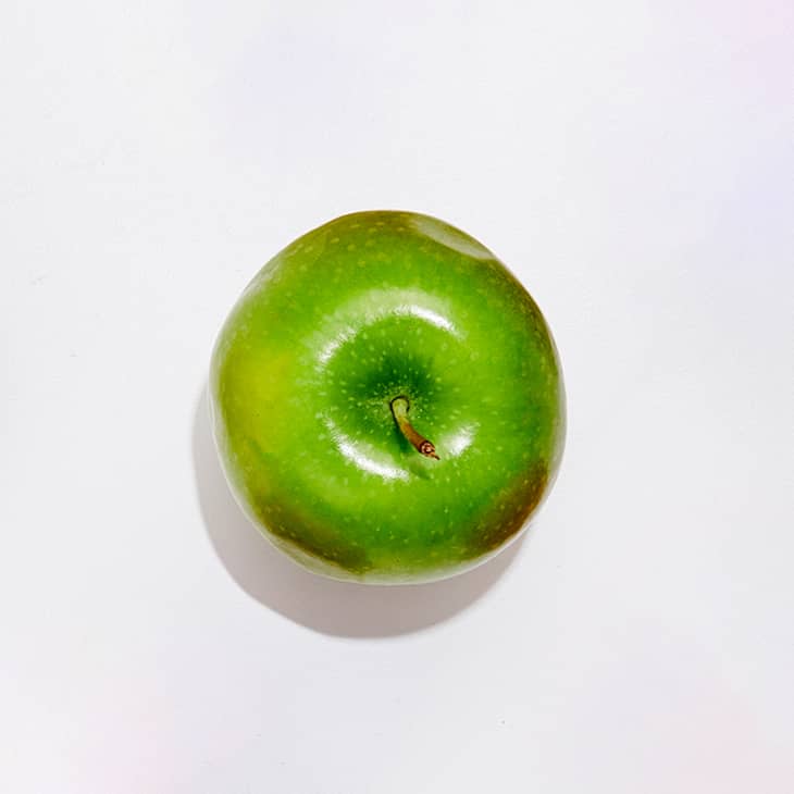 A Granny Smith apple on a white surface.