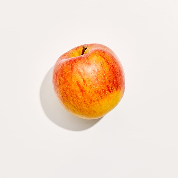 A braeburn apple on a white surface.